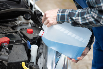 Hands of mechanic pouring windshield washer fluid in a car