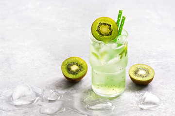 A refreshing summer drink with slices of kiwi and ice in a glass on a gray background. Selective focus.