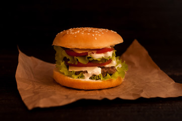 American burgers on tracing paper or food paper with tomatoes on a dark background
