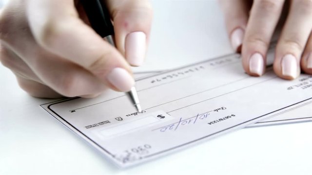 Close-up Of Hand Holding Pen Preparing Writing Check. Paycheck concept. Payment by cheque
