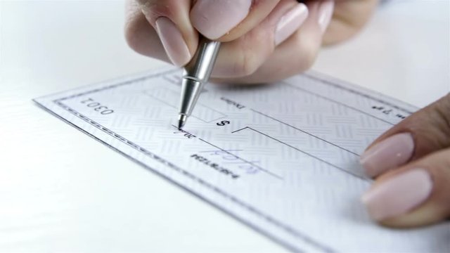 Female hand with pen filling a bank check. Paycheck concept. Payment by cheque