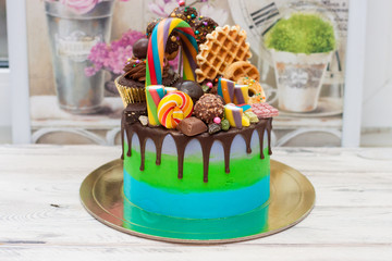 Blue and green cake with dark chocolate, cupcake, lollipops, cake pops, ferrero, waffle, candies and sprinkles.