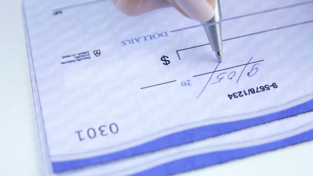 Close up of writing a check with a ball point pen. Paycheck concept. Payment by cheque