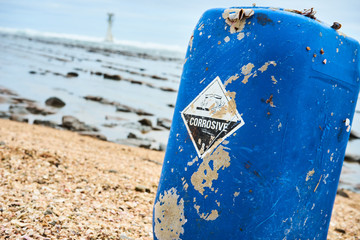 Naklejka premium Blue canister laying on a beach in japan with a chemical corosive sign on it demonstrating ocean pollution and environment pollution