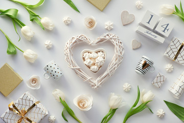 Valentines day flat lay, top view on white background with fresh tulips, coffee cups and sweets, copy-space. Valentine gift wrapped in paper with golden lines. Wood calendar with 14 February.