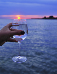 Female hand holds a wine glass on sea background.