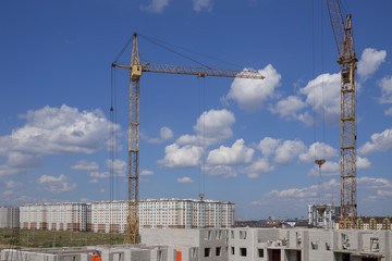 Construction site with cranes and building with cloudy sky background