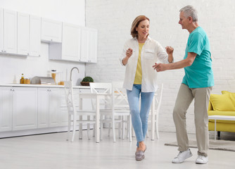 Fototapeta na wymiar Happy senior couple dancing in kitchen at home
