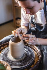 Potter working on a Potter's wheel making a vase. Woman forming the clay with her hands creating jug in a workshop.