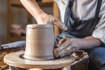 Potter working on a Potter's wheel making a vase. Woman forming the clay with hands creating jug in...