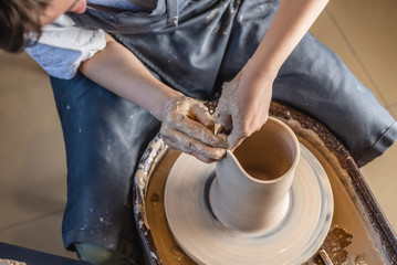 Woman potter working on Potter's wheel making a vase. Master forming the clay with her hands creating jug in a workshop