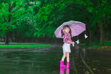 雨降りの暗い林を傘を差し笑顔で振り返る幼い女の子。