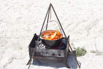 Tourist cooking meat with vegetables in a cauldron on the beach.