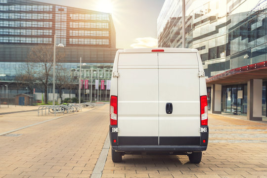 Small cargo delivery van driving in european city central district. Medium lorry minivan courier vehicle deliver package at residential office building in downtown area. Commercial shipping logistics