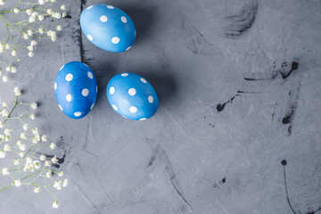 Bright blue polka dot eggs with white spring flowers on a gray background. Festive Easter card
