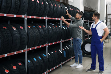Mechanic helping client to choose car tire in auto store
