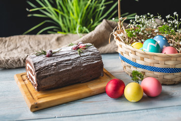 Festive Easter lunch with colorful bright eggs in a basket and an cake on a wooden table. Traditional spring holiday.