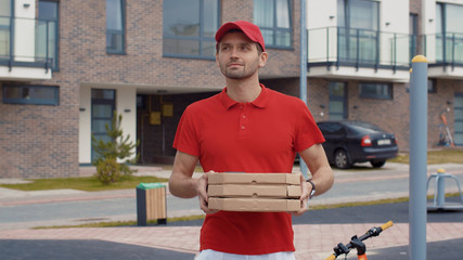 Handsome delivery man in red uniform carrying pizza boxes searching location customer house in...