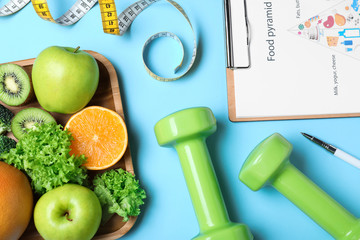 Fruits, dumbbells, measuring tape and list of products on light blue background, flat lay. Visiting...