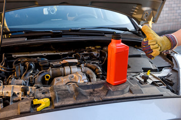 Fototapeta premium Oil change concept. Male hand in glove with oil bottle and car engine close up