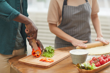 Close-up of young couple standing at the kitchen table and cooking together man cutting vegetables and woman making dough