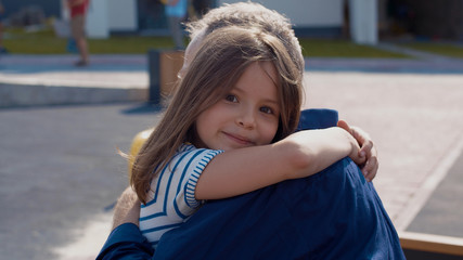 Pretty cute little girl running in the street hugging her smiling grandpa. Family portrait of cheerful child and elderly man spending spare time outdoors. Adorable family vibes.