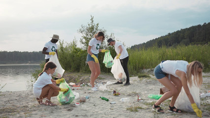 Save the planet. Team of vigorous recycling volunteers ccollecting plastic rubbish into bags on lake beach cleaning up nature landscape.
