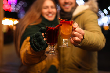 Happy couple with mulled wine at winter fair, focus on cups