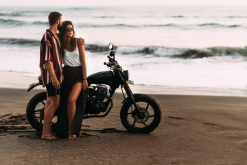 Couple on a motorcycle on the beach. A couple in love on the beach meets the sunset. A man embraces...