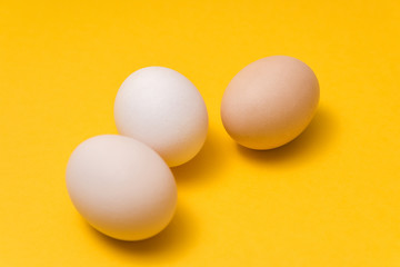 closeup of three natural color ecological eggs on yellow background randomly alined
