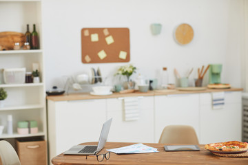 Image of wooden table with laptop and pizza on it in the empty kitchen at home