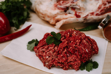 Fresh homemade minced meat from the legs of a ram. Cooking in the kitchen. Red minced lamb mince on a background of greens and red pepper, spices