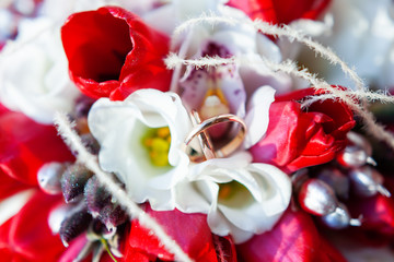 Golden wedding rings on bridal bouquet. Symbol of love and marriage on floral composition of bright red tulips.