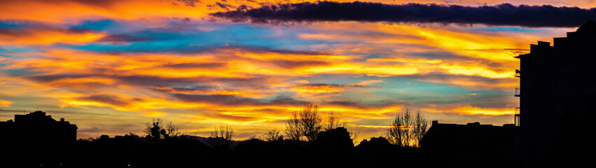Fototapeta na wymiar Panorama of colorful sunset sky over the silhouettes of houses