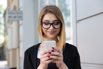 Good news. Woman wearing glasses business black wear jacket dress texting on the smart phone walking in the street in a sunny day office building on background