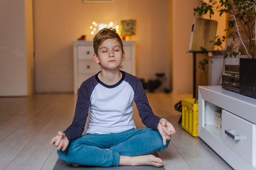 Little boy doing Yoga meditation exercises at home.