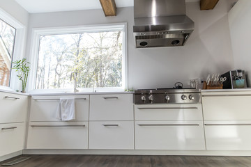 Fototapeta premium spacious large modern white kitchen recently updated with high end appliannces, wood floors, picture windows, white cabinets and wood beams and a great view of the backyard