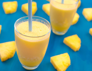 fresh pineapple juice in a glass with a straw on a blue and green background