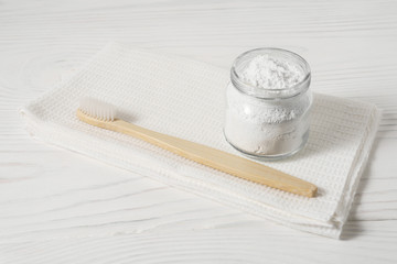 Bamboo toothbrush with a white textile towel and powder for cleaning teeth in a bowl on a light...