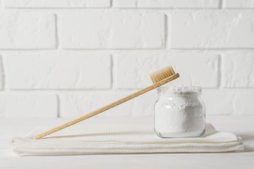 Bamboo toothbrush with a white towel and powder for cleaning teeth in a bowl on a background of a light brick wall. Horizontal orientation, image with copy space.