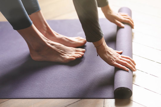 Concept of healthy lifestyle. Close up of young woman hands rolling violet yoga fitness mat before working out at home in living room. Every day morning ritual. Wooden floor, soft light