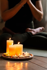 Close-up. Woman in yoga lotus pose meditating in a dark room with candle light. Atmosphere of relax...