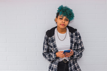 young brunette afro american girl with mobile phone on white brick wall