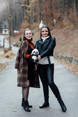 Two young beautiful teen girls in trendy clothes. Carefree women posing. Positive models having fun. Life style, happiness, emotional and people concept.   Girl posing with a panda toy