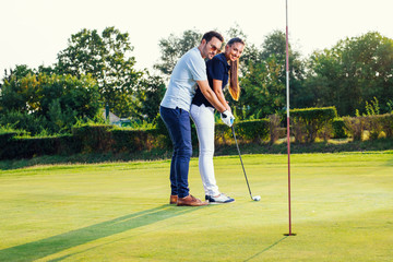 Young couple playing golf. Personal trainer giving lesson on golf course.