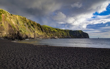 View on the beach with black volcanic sand and green hill, Sao Miguel Azores