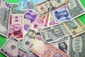 Fototapeta na wymiar Assorted paper money background. Mix of American, Chinese and Indian colorful banknotes in a bright green color background.