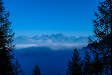 A moody mountain range of Lienz Dolomites, Austria, hiding in the mist. The valley is shrouded in fog. High mountain climbing. Freedom and solitude. There are no clouds in the higher parts