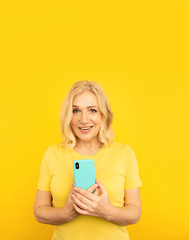 Happy adult female with blue mobile on the yellow background