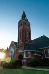 Red brick church with bell towe,r setting sun backlighting